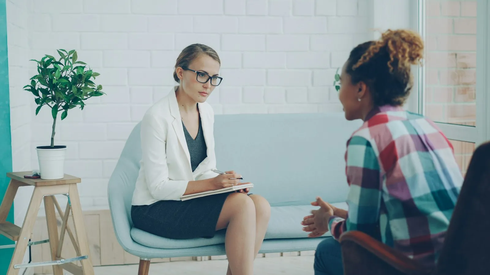 A clinician in conversation with a patient across a desk in a softly lit consulting room